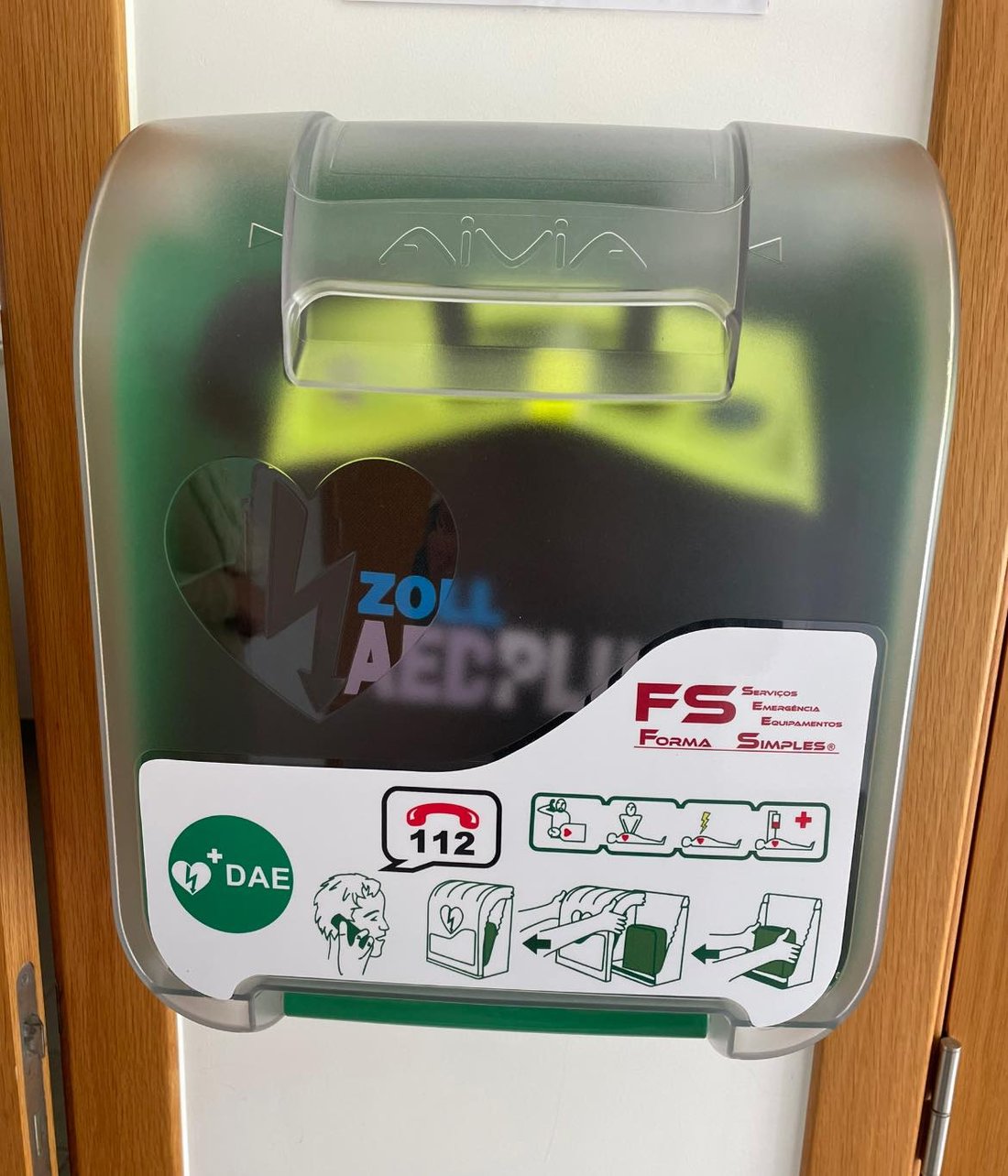 Armário DAE com desfibrilhador Zoll AED Plus instalado junto a uma porta, com sinalética e número de emergência 112